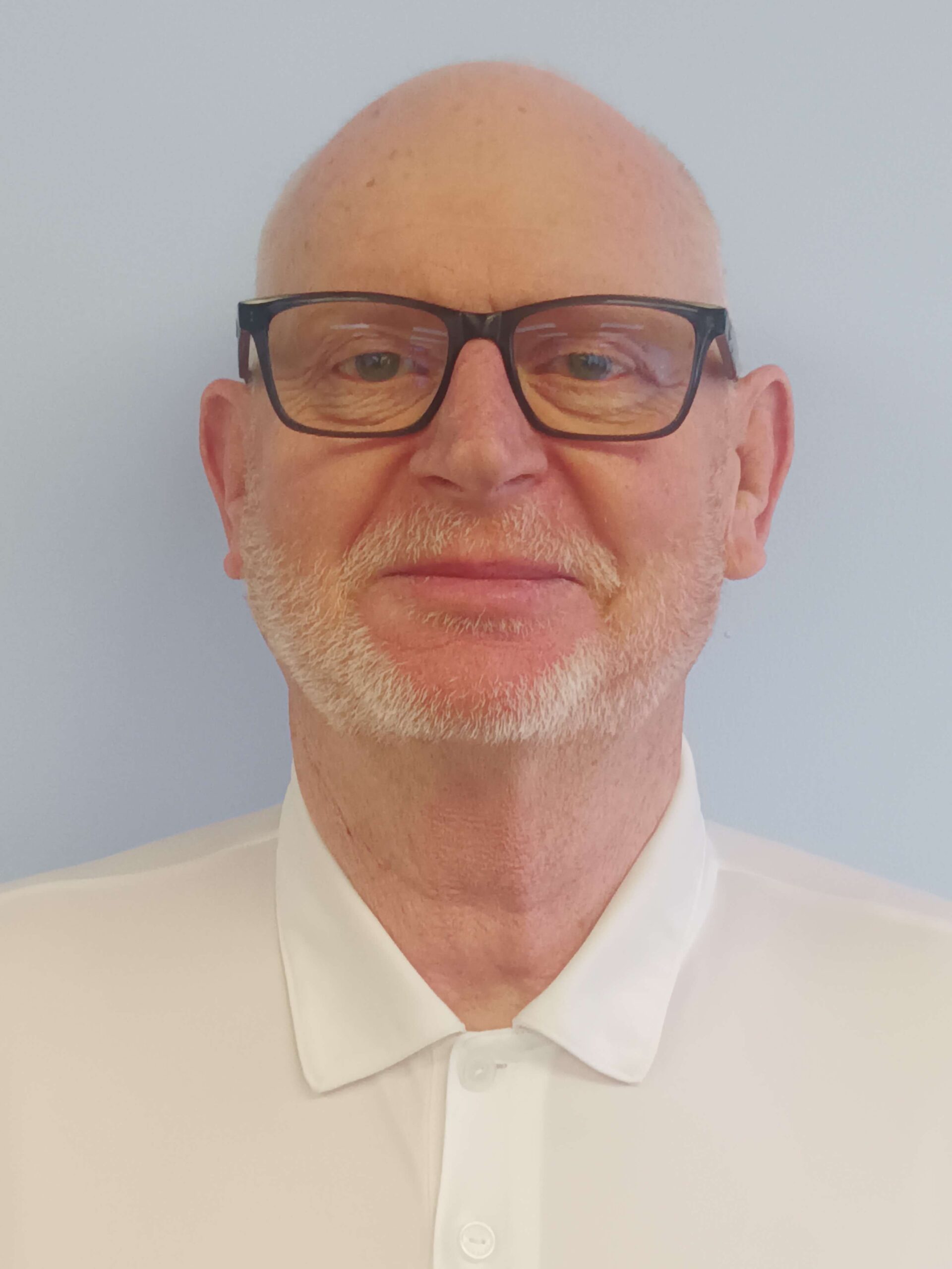 <br />
Sean McCrave CEO OI, a smiling man with glasses and a beard is wearing a dark blazer over a striped shirt. He stands against a light grey background.